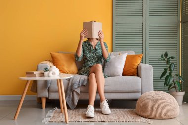 Evdeki kanepede yüzü kitapla kaplı güzel bir kadın.