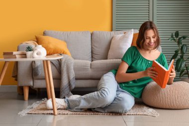Evdeki kanepenin yanında kitap okuyan güzel bir kadın.