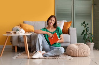 Evdeki kanepenin yanında kitap okuyan güzel bir kadın.