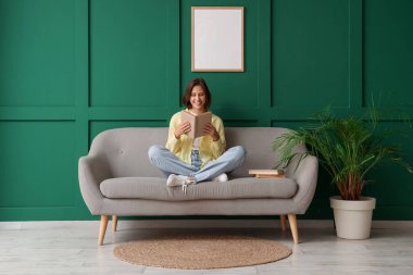 Yeşil duvarın yanındaki kanepede kitap okuyan güzel bir kadın.