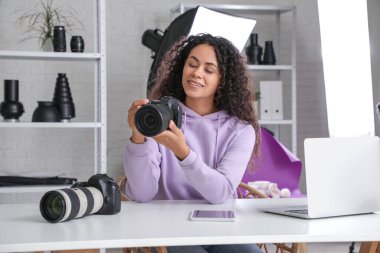 Kameralı Afro-Amerikalı bir fotoğrafçı stüdyoda masada oturuyor.