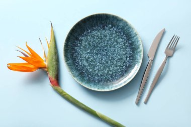 Mavi arka planda güzel bir strelitzia çiçeği ve çatal bıçak takımı.