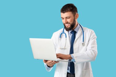 Mavi arka planda dizüstü bilgisayarı ve steteskopu olan mutlu bir erkek doktor.