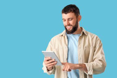 Mavi arka planda tableti olan yakışıklı, mutlu bir adam.
