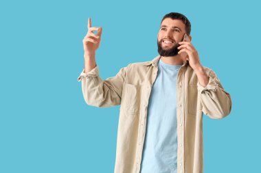 Yakışıklı genç adam mavi arka planda cep telefonuyla konuşuyor.