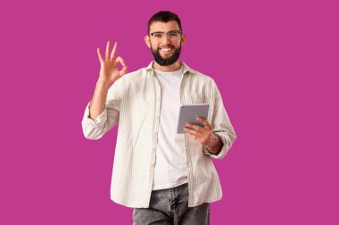 Tabletli yakışıklı genç adam mor arka planda iyi niyet göstergesi gösteriyor.
