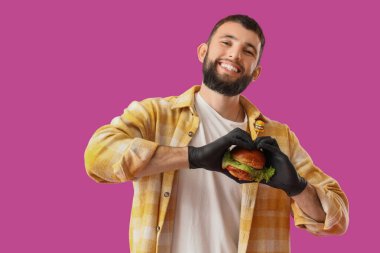 Pembe arka planda lezzetli burgeri olan genç adam.