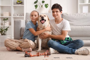 Mutlu kız ve erkek kardeş ve şirin Labrador köpeği evde yerde oturuyor.