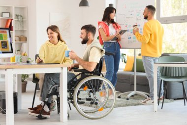 Kahve fincanı olan bir erkek tasarımcı ve iş arkadaşı ofiste çalışıyor.