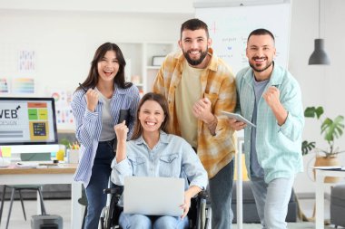 Ofiste tekerlekli sandalyedeki kadınla mutlu tasarımcılar.