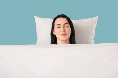 Yumuşak battaniyeli ve yastıklı güzel bir kadın mavi arka planda uyuyor.