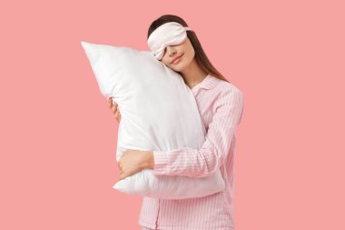 Maskeli güzel bir kadın pembe arka planda yastığa yaslanıyor.
