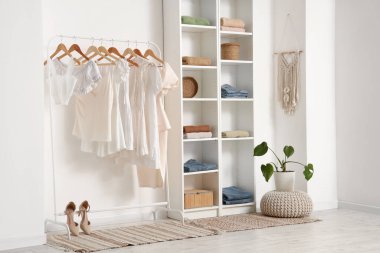 Farklı kadın kıyafetleriyle aydınlık soyunma odasının şık bir iç mekanı.