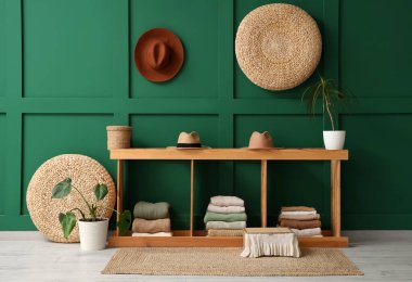 Katlanmış elbiseli ahşap askı, renkli duvarların yanında şapkalar ve bitkiler.