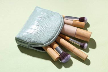 Yeşil arka planda farklı makyaj ürünleri olan kozmetik çanta.