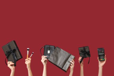 Ödeme terminali olan kadın elleri, hediye kutuları, alışveriş çantası ve kırmızı arka planda makyaj fırçaları. Kara Cuma İndirimi