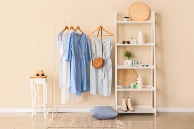 Farklı şık kıyafetler ve bej duvarın yanında aksesuarlı raflar.