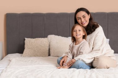 Küçük kız ve annesi sıcak kazaklar içinde yatak odasında oturuyorlar.