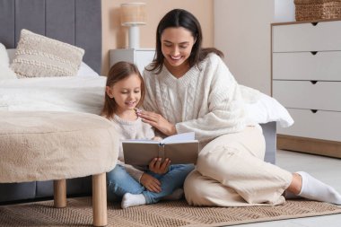 Anne ve küçük kızı yatak odasında oturmuş kitap okuyorlar.