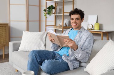 Yakışıklı genç adam evde kanepede kitap okuma
