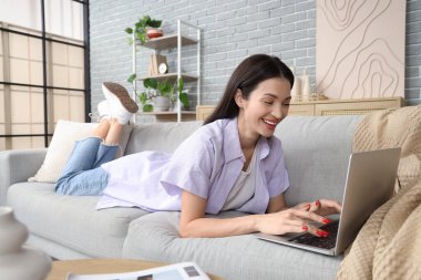 Evdeki kanepede dizüstü bilgisayar kullanan güzel genç bir kadın.