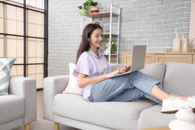 Evdeki kanepede dizüstü bilgisayar kullanan güzel genç bir kadın.