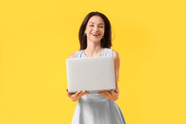 Sarı arka planda dizüstü bilgisayarı olan güzel genç bir kadın.