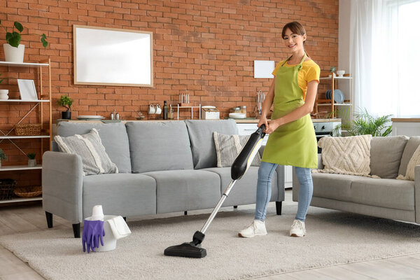 Pretty young woman with vacuum cleaner cleaning carpet at home