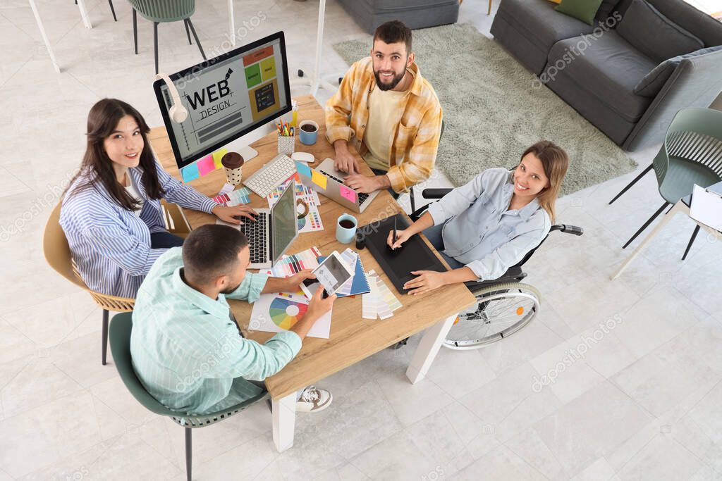 Team of designers with woman in wheelchair working at office, top view