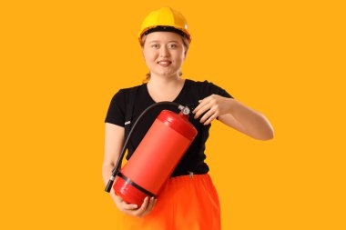 Sarı arka planda yangın söndürücü olan genç bayan itfaiyeci. Erkek mesleği kavramındaki kadın.