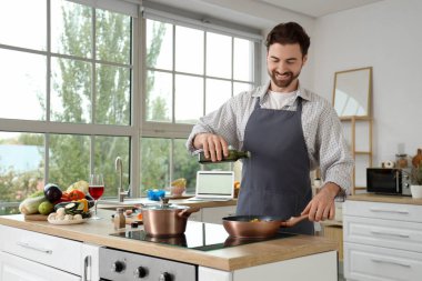 Yakışıklı sakallı adam mutfakta kızarmış sebzelerin üzerine zeytinyağı döküyor.