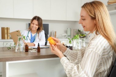Homeopatik doktorun muayenehanesinde elinde ilaç şişesi olan olgun bir kadın.