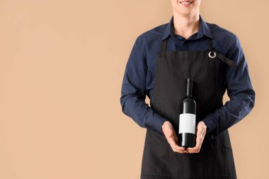 Bej arka planda bir şişe şarabı olan genç bir erkek garson.