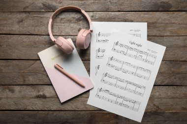 Müzik kağıtları, modern kulaklıklar, tahta arka planda defter ve kalem.