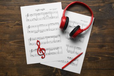 Müzik kağıtları, modern kulaklıklar, tahta arka planda kalem ve keman anahtarı.