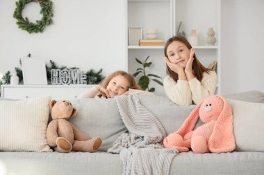 Kanepenin arkasında sevimli kız kardeşler ve evde oyuncaklar.