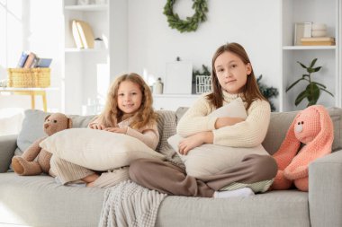 Yastıkları ve oyuncakları olan sevimli kız kardeşler kış günü evde oturuyorlar.