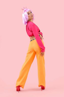 Mor peruklu güzel, genç ve mutlu bir kadın ve pembe arka planda taç.