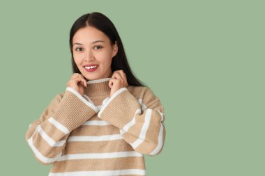 Yeşil arka planda kalın kazaklı güzel bir kadın.