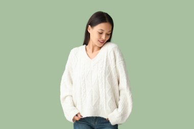 Yeşil arka planda beyaz örgü süveter giyen güzel bir kadın.