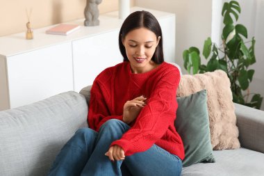 Evdeki kanepede oturan kırmızı örgü süveterli güzel genç kadın.