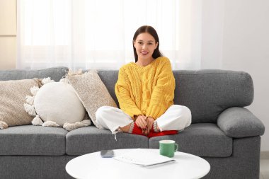 Sarı örgü süveterli güzel bir kadın evdeki kanepede oturuyor.