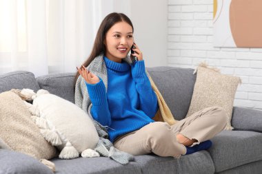 Mavi örgü süveterli, kanepeye oturmuş, cep telefonuyla konuşan güzel bir kadın.