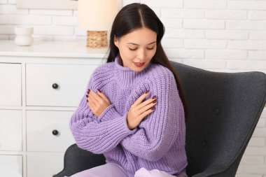 Leylak örgülü süveter giymiş güzel bir kadın evdeki koltukta oturuyor.