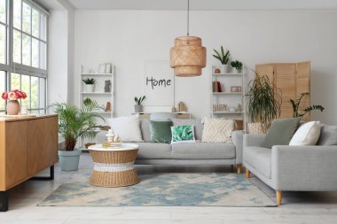 Gri koltukları, raf üniteleri ve bitkileri olan oturma odasının içinde.