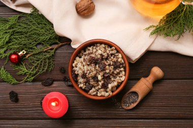 Bir kase geleneksel Ukrayna Kutya yemeği, kozalaklı dallar ve ahşap zemin üzerinde yanan mum.