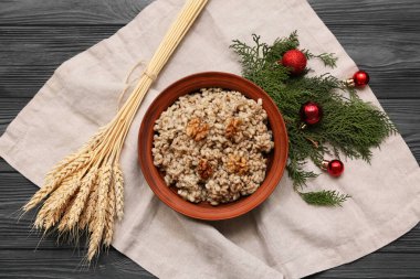 Bir kase geleneksel Ukrayna Kutya yemeği, kozalaklı dallar ve siyah ahşap arka planda Noel topları.