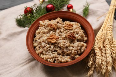 Bir kase geleneksel Ukrayna Kutya yemeği, kozalaklı dallar ve siyah ahşap arka planda Noel topları.