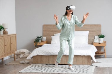 Evde VR gözlük takan yeşil pijamalı genç bir kadın.