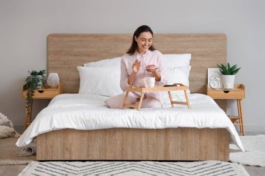 Çizgili pijamalı genç bir kadın evde kahvaltı yapıyor.